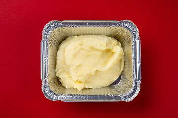 Mashed potatoes in disposable packaging for delivery on a red background.
