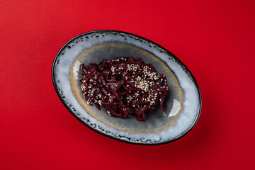 Grated beets with sesame on a plate on a red background