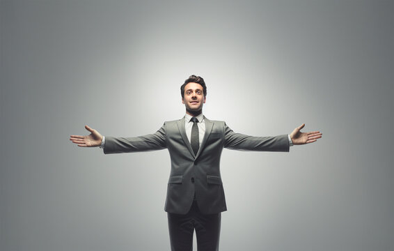 Businessman with arms open wide, welcoming gesture. On grey background.