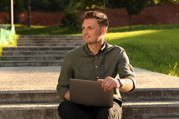 Obraz premium Handsome man with laptop sitting on concrete stairs outdoors
