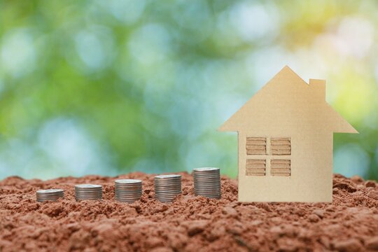 Model of a house with coins lying on the ground and natural green background, under the concept of saving money to buy a house