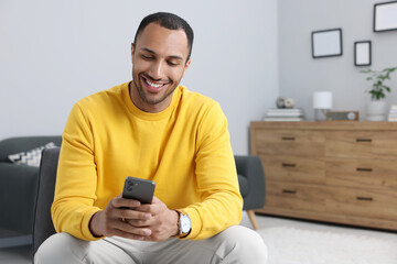 Happy man sending message via smartphone indoors