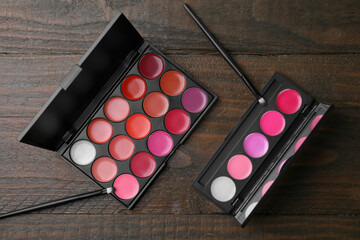 Colorful lipstick palettes with brushes on wooden table, flat lay. Professional cosmetics