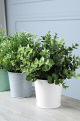 Different artificial potted herbs on white wooden table