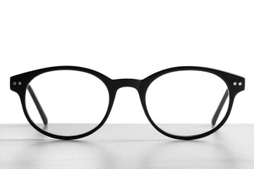 Stylish glasses with black frame on table against white background