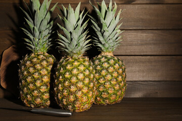 Whole ripe pineapples and knife on wooden table