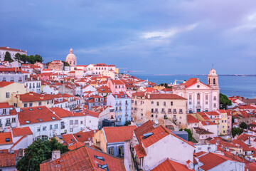 Obraz premium View of Lisbon famous view from Miradouro de Santa Luzia tourist viewpoint over Alfama old city district on sunset with dramatic overcast sky. Lisbon, Portugal.