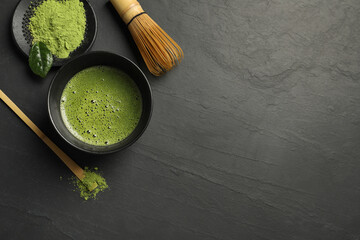 Cup of fresh matcha tea, bamboo whisk, spoon and green powder on black table, flat lay. Space for...