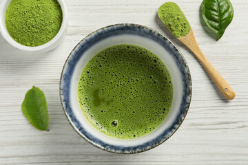 Cup of fresh matcha tea, green powder and leaves on white wooden table, flat lay