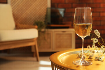 Glass of white wine and flowers on table in room, space for text. Relax at home