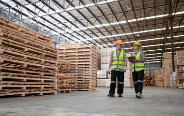 Fototapeta premium Engineer team standing walking in warehouse examining hardwood material for wood furniture production. Technician man and woman working on quality control in lumber pallet factory. Worker check stock