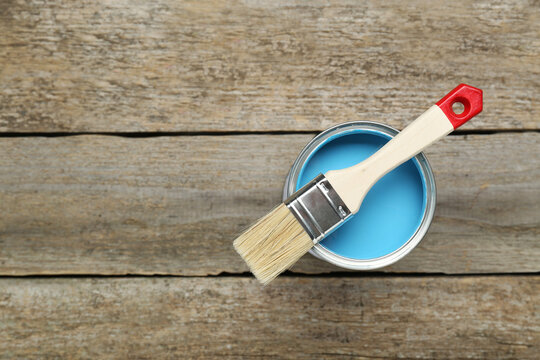 Can of light blue paint with brush on wooden table, top view. Space for text