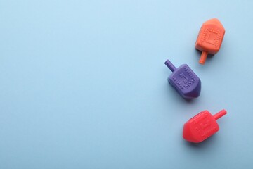 Colorful dreidels on light blue background, flat lay with space for text. Traditional Hanukkah game
