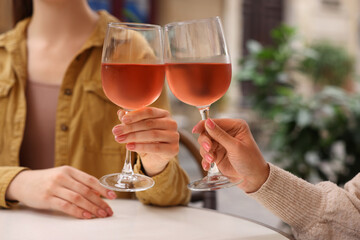 Women clinking glasses with rose wine at white table in outdoor cafe, closeup