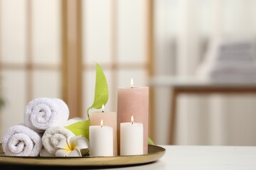 Fototapeta na wymiar Spa composition. Burning candles, plumeria flower, green leaves and towels on white table indoors, space for text