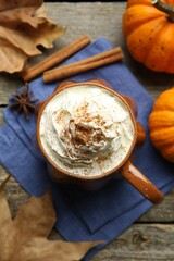 Mug of pumpkin spice latte with whipped cream, ingredients and dry leaves on wooden table, flat lay