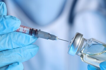 Doctor inserting syringe into glass vial with medication, closeup
