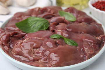 Plate of raw chicken liver with basil on white table, closeup