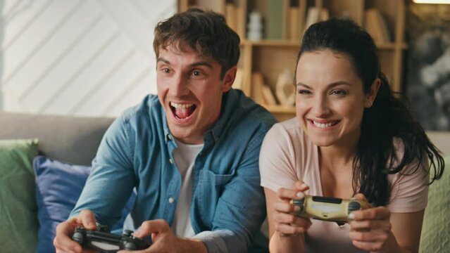 Smiling players enjoy video games sitting couch close up. Couple playing online