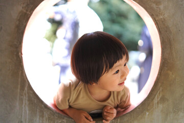 公園の遊具の窓を覗く男の子/Boy looking through window of playground equipment in park