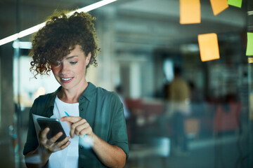 Happy young businesswoman using a smartphone in the office - obrazy, fototapety, plakaty