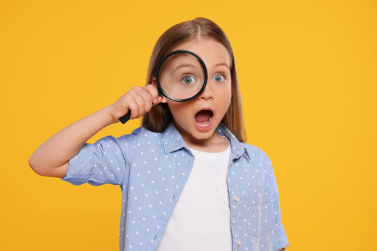 Cute little girl looking through magnifier on yellow background