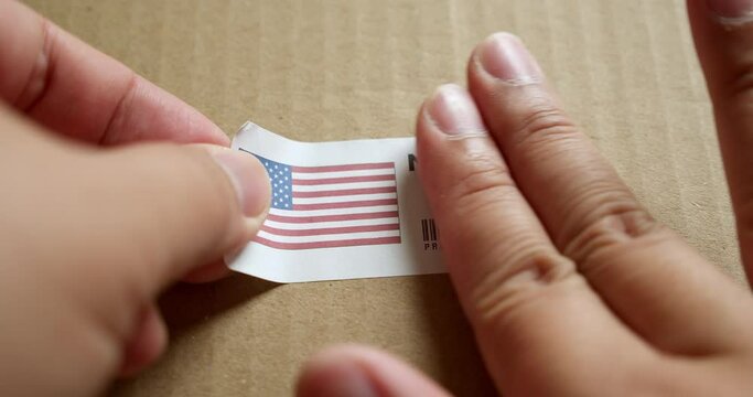 Hands applying MADE IN USA flag label on a shipping box with product premium quality barcode. Manufacturing and delivery. Product factory import and export.