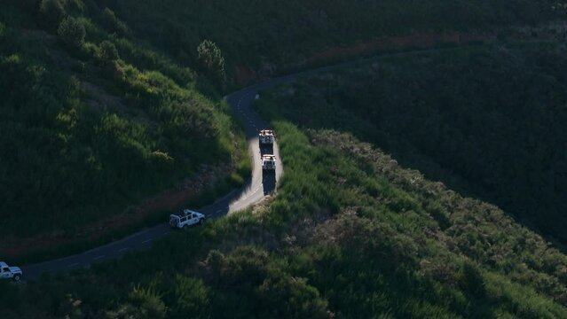 Aerial drone shot of 4 white jeep vehicles convoy driving through winding mountain road in Madeira island. Sunny daytime shot.