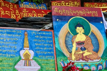 Vibrant Tibetan Buddhist prayer stones and a beautifully painted depiction of Buddha create a...