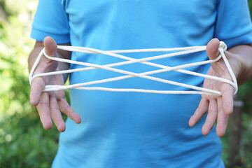 Closeup man hands is playing rope which called cats cradle game. Concept, game involving the creation of various style figures between the fingers. Traditonal playing.                                - obrazy, fototapety, plakaty