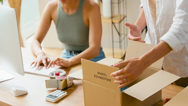 Close up of two women running online fashion business start up from home taking and sealing orders in box for distribution - shot in slow motion