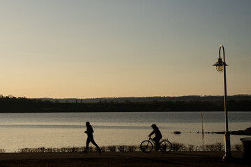 people exercising around the lake in the park at sunset