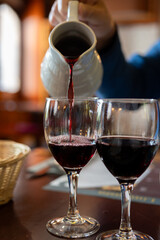 Pouring yound red beaujolais wine in glass during celebration of end of harvest and first sale release on third Thursday of November from white ceramic pitcher in Limouges, France