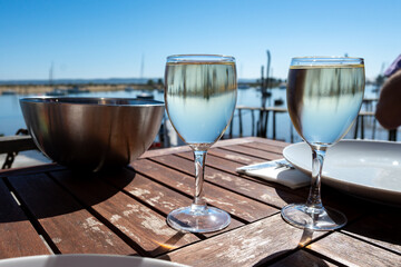 Drinking of white wine at farm cafe in oyster-farming village, with view on boats and water of Arcachon bay, Cap Ferret peninsula, Bordeaux, France