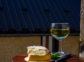 Reblochon French cheese made in Haute-Savoie, white Roussette de Savoie or Vin de Savoie wine with view on old alripne village and Hautes Alpes mountains snow tops in summer