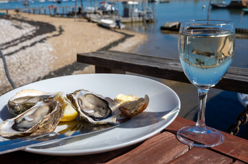 Eating of fresh live oysters with glass of white wine at farm cafe in oyster-farming village, with...