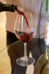 Sommelier or waiter pouring of burgundy red wine from grand cru pinot noir vineyards, glass of wine and view green vineyards in Burgundy Cote de Nuits wine region