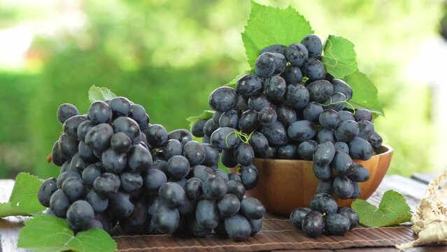 Bunch of Black grapes with leaves in Bamboo basket on wooden table in garden, Black or Purple grape with leaves in blur background.