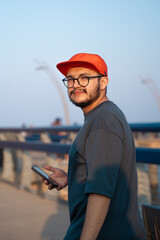 young guy with a red hat and grey T-shirt, walking with a phone in his hands, enjoying the sunset