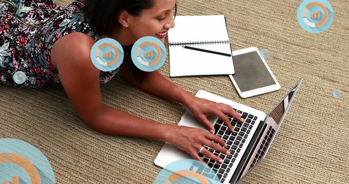 Animation of graph icon in circles over biracial woman lying on floor and using laptop