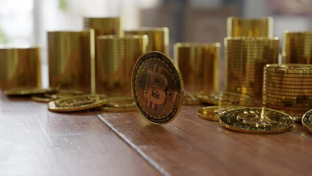 Focus on a single bitcoin spinning on a wooden table and stacks of bitcoins behind it