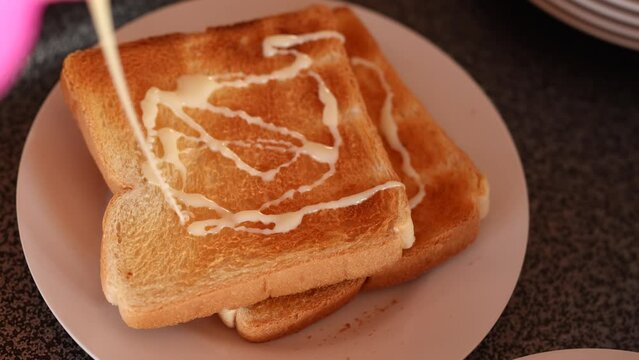 Female hand squeezing condensed milk onto toast