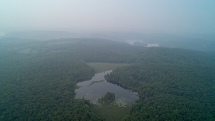 An aerial view of a forest, pond and lake on a hazy day due to wildfires