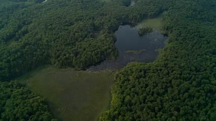 Looking down from an aerial view of a forest and pond in the country during a hazy sunset because of wild forest fires