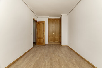 Empty bedroom with a built-in wardrobe with two oak wood doors with handles, a skirting board of...