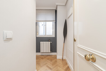 Hallway and hallway of a residential apartment with oak parquet floors, window to the interior patio with aluminum radiator below and smooth walls painted white and gray