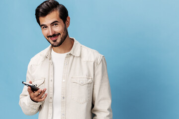 Portrait of a brunette man with a phone in his hands smiling on a blue background in a white...