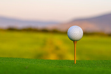 Golf ball is on tee at green lawn in a beautiful golf course with morning sunshine.