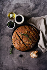 Freshly baked sourdough bread from whole grain flour and pumpkin seeds on a grid, olive oil and black olive on a rustic wooden table. Artisan bread.