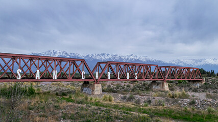 Vemos un viejo puente de ferrocarril , puro hierro forjado cruzando el rio Tunuyan , en el...
